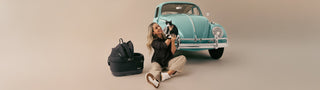 Woman with a dog and Tavo pet car seat in front of a vintage teal car on a beige background