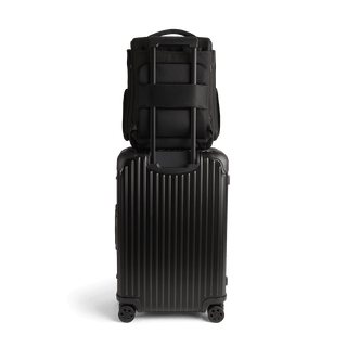 A Kamella Pet Backpack and Car Seat, in onyx, from the back attached to a suitcase using the trolley sleeve.