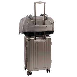 back view of compact, gray pet car seat with two carry handles on top sitting on a silver, hardshell suitcase, secured with the carrier's trolley sleeve - view 6