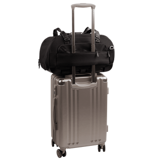 back view of compact, black pet car seat with  two carry handles on top sitting on a silver, hardshell suitcase, secured with the carrier's trolley sleeve - view 7
