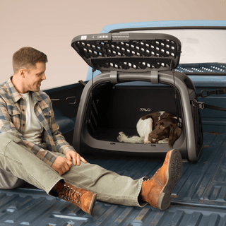 A man sitting in the bed of a pickup truck next to the Everett L pet cargo crate installed into the vehicle with a dog laying in it 