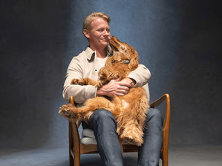 Man sitting on a chair holding a dog against a blue background
